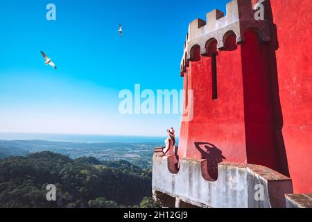 Junge, unbeschwerte Touristenfrau in weißem Kleid und Sonnenhut, die auf dem Balkon steht und einen schönen Blick auf Sintra, Portugal, genießt. Sommerurlaub. Stockfoto