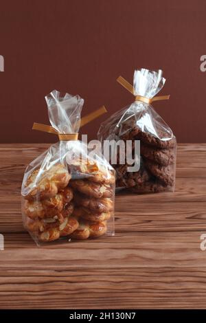 Schokoladen-Haferflocken-Kekse und Shortbread-Kekse mit Mandelflocken in transparenten Tüten auf einem Holztisch. Nahaufnahme Stockfoto