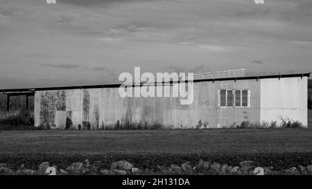 Eine alte Wellblech-Landschuppe auf einem ländlichen Grundstück in schwarz-weiß Stockfoto