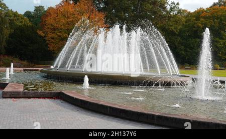 Der Kurpark von Bad Oeynhausen, Deutschland, hat einen großen Brunnen in der Mitte. Im Hintergrund Bäume, die beginnen, ihre Herbstfarben zu bekommen. Stockfoto