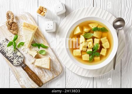 Zuppa imperiale, italienische Suppe aus Hühnerbrühe mit Parmesan-Eierknödeln, bestreut mit geriebenem Käse und Basilikum in einer weißen Schüssel auf einem Holztisch wi Stockfoto