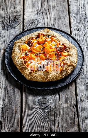 Kürbisgalette mit karamellisierter Zwiebel und zerbröseltem Fetakäse auf einer schwarzen Platte auf einem rustikalen Holztisch, vertikale Ansicht von oben Stockfoto