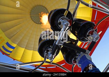 Heißluftballon-Pilot hat seine Hand auf dem Gasbrenner und füllt heiße Luft in einen gelben Ballon Stockfoto