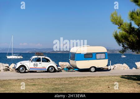 Herbie VW Käfer Auto mit einem alten Adria Anhänger, der am Meer neben einer Kiefer steht Stockfoto