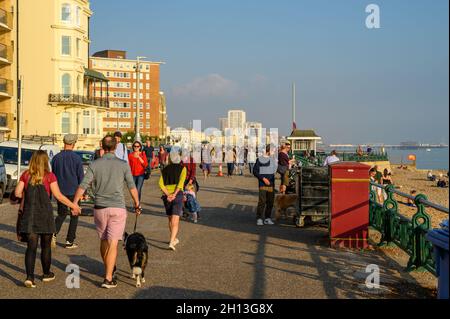 Menschen, die bei strahlendem Oktobernachmittagssonne auf der Hove-Promenade mit Blick auf Brighton im Hintergrund spazieren. East Sussex, England. Stockfoto