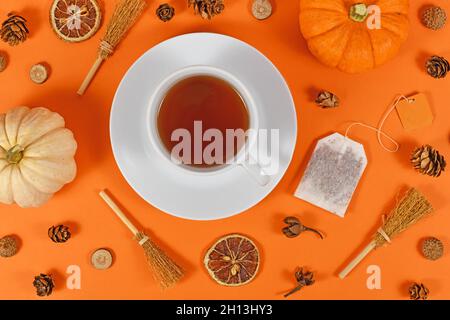 Tasse Tee umgeben von saisonalen Herbstdekorationen wie Kürbissen und orangefarbenen Scheiben auf orangefarbenem Hintergrund Stockfoto