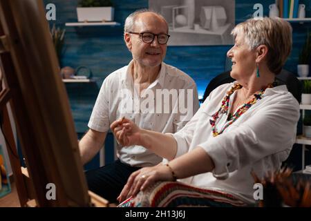 Ältere Künstler, die im Kunststudio über die Erstellung von Zeichnungen sprechen. Kaukasisch gealterte Männer und Frauen diskutieren Meisterwerk in professionellen Kunstraum. Seniorenpaar mit künstlerischer Phantasie Stockfoto