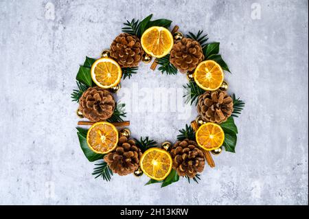 Festlicher Weihnachtskranz oder Adventskrone aus getrockneten Orangenscheiben, Tannenzapfen, Weihnachtskugeln oder Kugelschmuck, Zimtstangen, grünes Efeu, Tannengrün Stockfoto