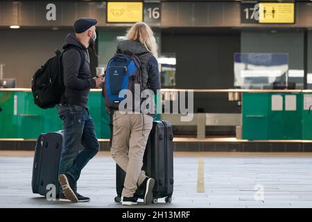 Schkeuditz, Deutschland. Oktober 2021. Reisende warten mit ihrem Gepäck beim Check-in am Flughafen Leipzig/Halle. Das erste Wochenende der Herbstferien in Sachsen ist eine geschäftige Zeit am Flughafen. Insgesamt starten am Samstag und Sonntag 50 Flugzeuge von den Flughäfen Leipzig/Halle und Dresden in Sachsen zu Urlaubszielen wie Spanien, der Türkei, Griechenland und Italien. Kredit: Peter Endig/dpa-Zentralbild/dpa/Alamy Live Nachrichten Stockfoto