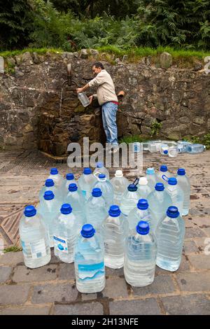 Großbritannien, England, Worcestershire, West Malvern, Mann am Auslauf, der Gallonen-Flaschen bei Hay Slad Spring mit Wasser füllt Stockfoto