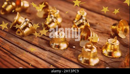 Bild von Sternen, die über weihnachtsglocken auf Holzflächen fliegen Stockfoto