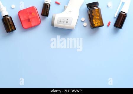 Grippebehandlungen. Nasensprays, Pillen zur Behandlung von Erkältungen, Digitalthermometer auf pastellblauem Hintergrund. Flach liegend, Draufsicht, Kopierbereich. Stockfoto