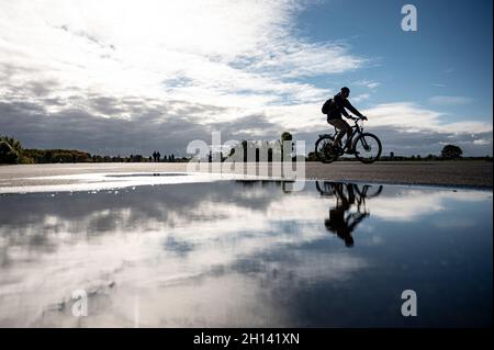 Berlin, Deutschland. Oktober 2021. Ein Radfahrer spiegelt sich in einer Pfütze auf dem Tempelhofer Feld wider. Quelle: Fabian Sommer/dpa/Alamy Live News Stockfoto