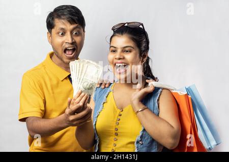 Indisches Paar in gelbem Kleid mit Einkaufstaschen und indischen Währungen lächeln auf weißem Hintergrund Stockfoto