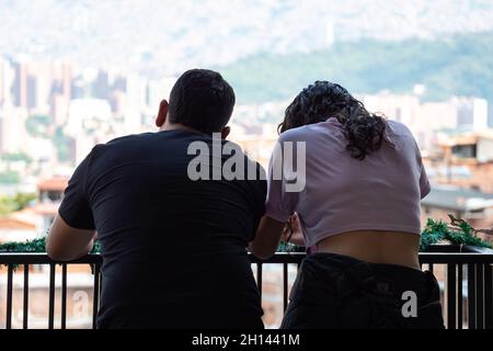 Ein Paar, das sich auf dem Geländer eines Balkons anlehnend den Blick auf die Kommune 13, ein Touristenviertel in Medellin, Kolumbien, betrachtet Stockfoto