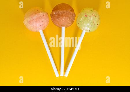 Satz Lutscher auf gelbem Hintergrund. Große helle leckere Lutscher auf weißen Stäben auf gelbem Hintergrund mit Kopierraum. Süßigkeitenkonzept Stockfoto