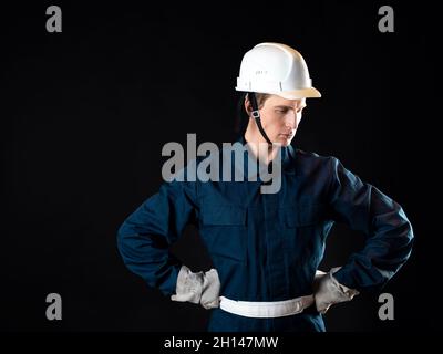 Ein Baumeister oder Mechaniker, ein Mann in einer Robe und einem Schutzhelm auf seinem Kopf, ein Foto auf schwarzem Hintergrund Stockfoto