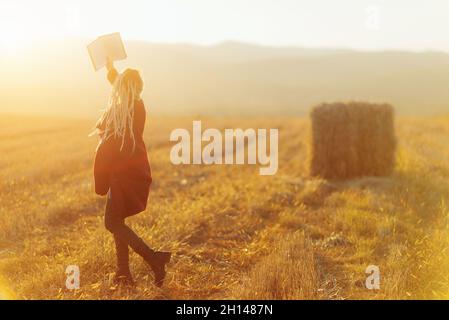 Eine fröhliche junge Frau liest ein Buch auf dem Land Stockfoto