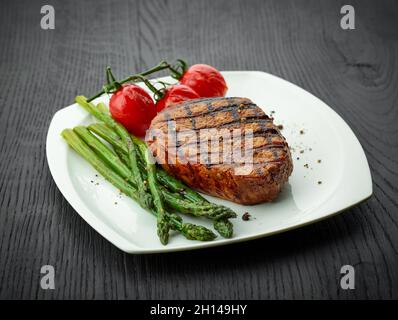 Frisch zubereitetes Kalbssteak, Tomaten und Spargel auf weißem Teller Stockfoto