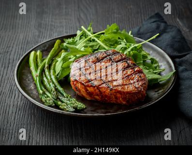 Frisch zubereitetes Kalbssteak, Spargel und Rucola auf dunklem Teller Stockfoto