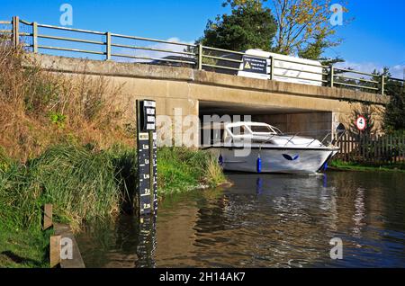 Ein Kreuzer, der unter der Ludham Bridge auf dem Fluss Ant auf den Norfolk Broads mit einem Auto und einem Wohnwagen in Ludham, Norfolk, England, Großbritannien, vorbeifährt. Stockfoto