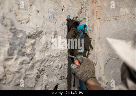 Arbeiter mit Kelle Verputzzement an der Wand mit PVC-Wasserleitung in renovierten Badezimmer verfällt Stockfoto