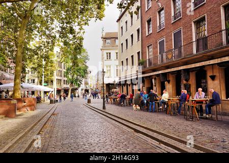 Düsseldorfer Altstadt mit Kopfsteinpflaster und Menschen, die vor einem Bierlokal im Freien sitzen. Die Altstadt ist ein beliebtes Touristengebiet. Stockfoto