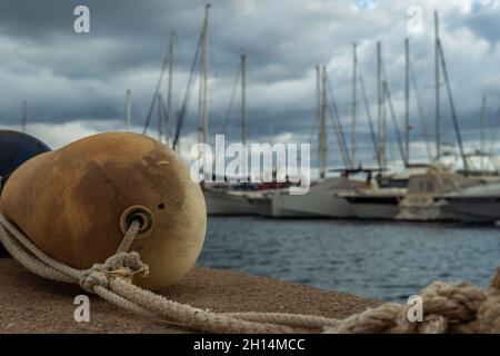 Nahaufnahme einer Plastikkugel in einem Hafen und im Hintergrund, unscharf, einer Marina auf der Insel Mallorca, bei einem bewölkten Sonnenuntergang Stockfoto