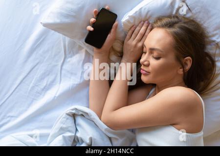 Foto einer Frau im Bett mit einem Smartphone. Zusatzkonzept für soziale Netzwerke. Blick von oben. Stockfoto