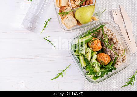 Lunchbox gefüllt mit Haferflocken, Gurkensalat und Nüssen, Brot, Birne auf weißem Holzhintergrund. Lunchbox Dinner. Draufsicht, flach liegend Stockfoto