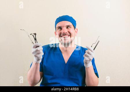 Junger lächelnder Arzt mit medizinischen Instrumenten in der Hand in grünem Chirurgenanzug isoliert Stockfoto