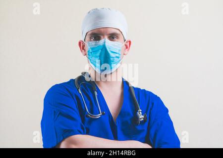 Junger Arzt Porträt in blauem Anzug mit Stethoskop und mit seinen Händen auf der Brust isoliert auf glattem Hintergrund Stockfoto