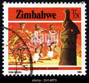 SIMBABWE - UM 1985: Eine in Simbabwe gedruckte Marke zeigt Zimbabwe Vogel und traditionellen Tanz, Erbe, um 1985 Stockfoto