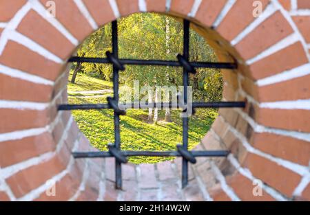 Herbstpark durch ein rundes Fenster mit einem geschmiedeten Gitter. Stockfoto