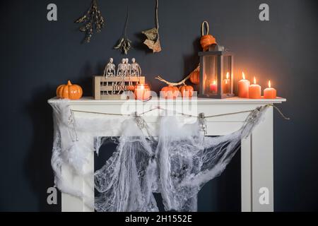 Halloween-Heimtextilien. Plastikspielzeug-Skelette in einer Holzkiste auf einem Kamin vor einer dunkelblauen Wand. Eine Girlande aus Skeletten. Spinnennetz auf dem Kleid Stockfoto