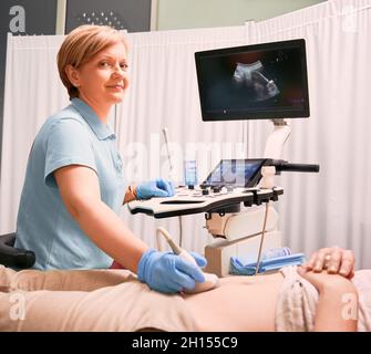 Ärztin in sterilen Handschuhen, die Frau mit Ultraschallscanner untersucht. Konzept der medizinischen Untersuchung, der weiblichen Gesundheit und der Ultraschalldiagnostik. Stockfoto