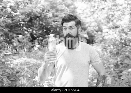 Jogging Trinkwasser. Guy hält den Körper Wasserhaushalt. Hydratation. Täglich Wasser. Erstaunt bärtigen Mann zeigen Flasche. Reife Hipster mit Bart im Wald. Stockfoto