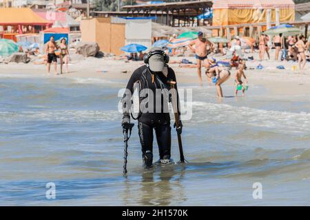 Ein Mann mit einem speziellen Gerät und Ausrüstung Metalldetektor auf der Suche nach verlorenen Schmuck und Gold im Meerwasser in der Nähe des Strandes. Stockfoto