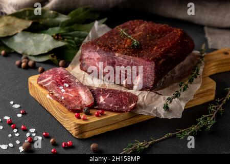 Stillleben Komposition mit einem Stück roten geräucherten trockenen Schinken auf einem hölzernen Schneidebrett, Seitenansicht Stockfoto