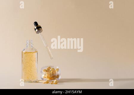 Gelserum in einer Glasflasche mit Pipette und Kapseln mit Serum zur Hautpflege von Gesicht, Augen und Körper in einem Behälter auf beigem Hintergrund. Stockfoto