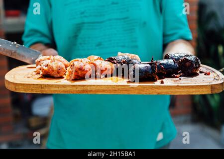 Argentinischer Steakhouse-Mann, der einen Tisch mit Chorizos ​​and Blutwurst zum Servieren trägt. Stockfoto