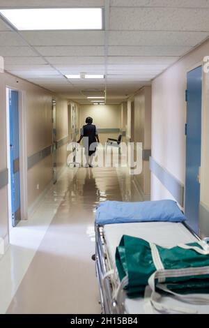 Allgemeiner Krankenhausflur, mit einem Bett, das auf einen Patienten wartet, afrikanische Krankenschwester, die geht Stockfoto