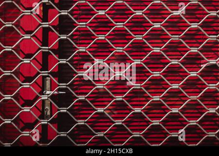 Eisenstruktur eines Stahlgrills auf roten Fensterläden an der Tür. Roter Hintergrund. Draußen Stockfoto