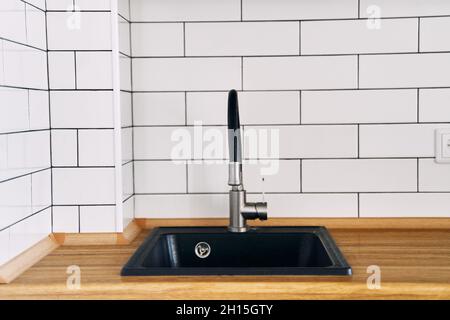Stilvolles schwarzes Waschbecken und Wasserhahn auf einer hölzernen Arbeitsplatte in einer Kücheneinrichtung aus nächster Nähe Stockfoto