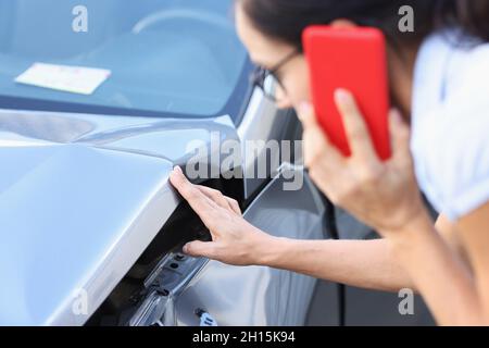 Die Fahrerin spricht auf dem Smartphone und untersucht Schäden am Auto nach der Nahaufnahme eines Unfalls Stockfoto