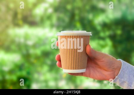 Umweltfreundliche Papierkaffeetasse in der Hand auf grünem Naturhintergrund mit Platz zum Kopieren Stockfoto