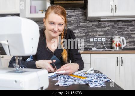 Heimnähkonzept. Junge Frau iis schneidet Stoff und schaut auf die Kamera. Horizontal. Stockfoto