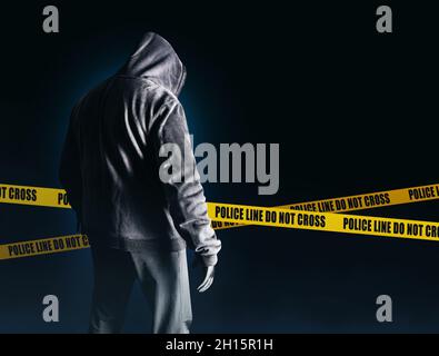 Foto von gruseligen Horror fremden Stalker Mann in schwarzer Kapuze und Kleidung auf dunkelblauem Hintergrund mit Polizei Linien. Stockfoto