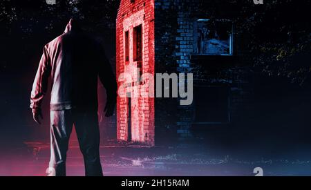 Foto von unheimlich Horror fremden Stalker Mann in schwarzer Kapuze und Kleidung auf verlassenen rot glühenden Gebäude Hintergrund. Stockfoto