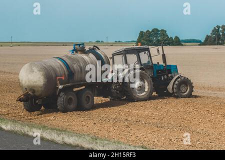 Traktor mit einem Fass Dünger auf dem Feld. Landwirtschaftliche Geräte und industrielle Arbeiten auf dem Bauernhof. Stockfoto